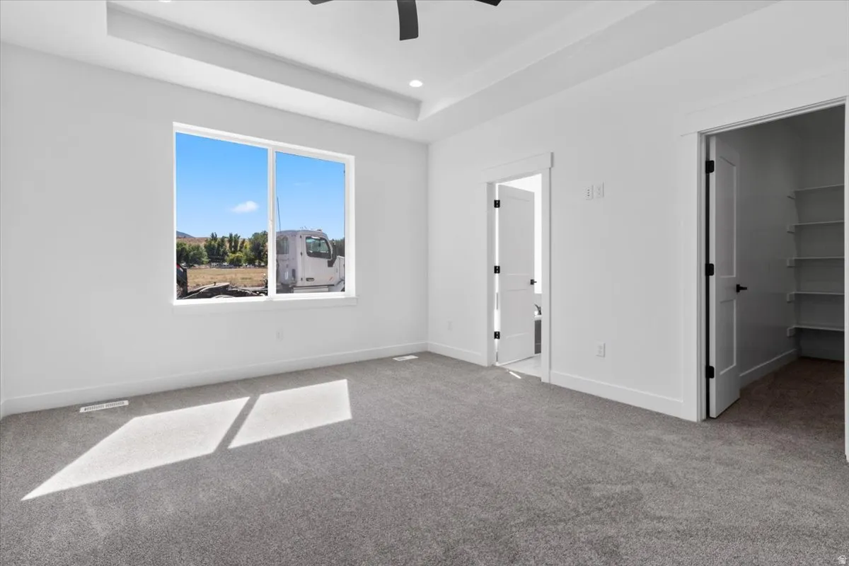 Tray ceiling with recessed lighting, large window, carpet flooring, flat panel interior doors, and built-in shelving