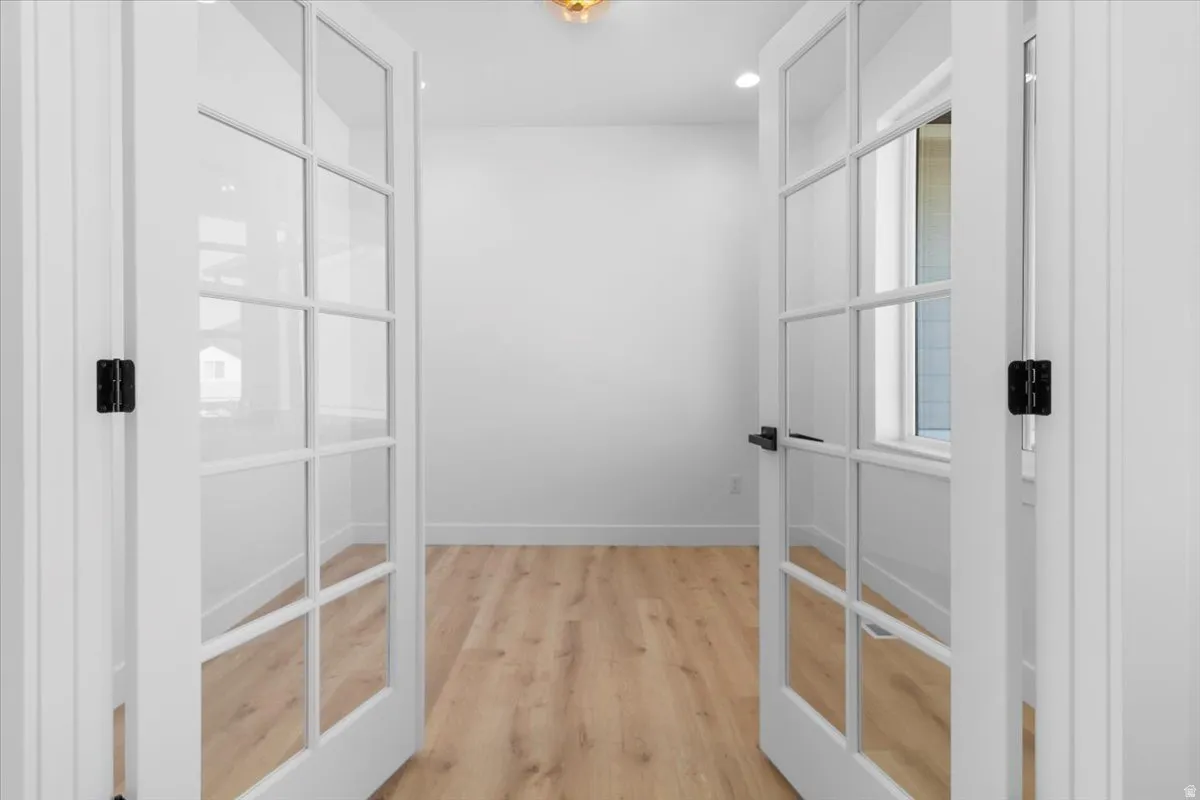 French doors with matte black hardware, wood-finish flooring, and a window for natural light