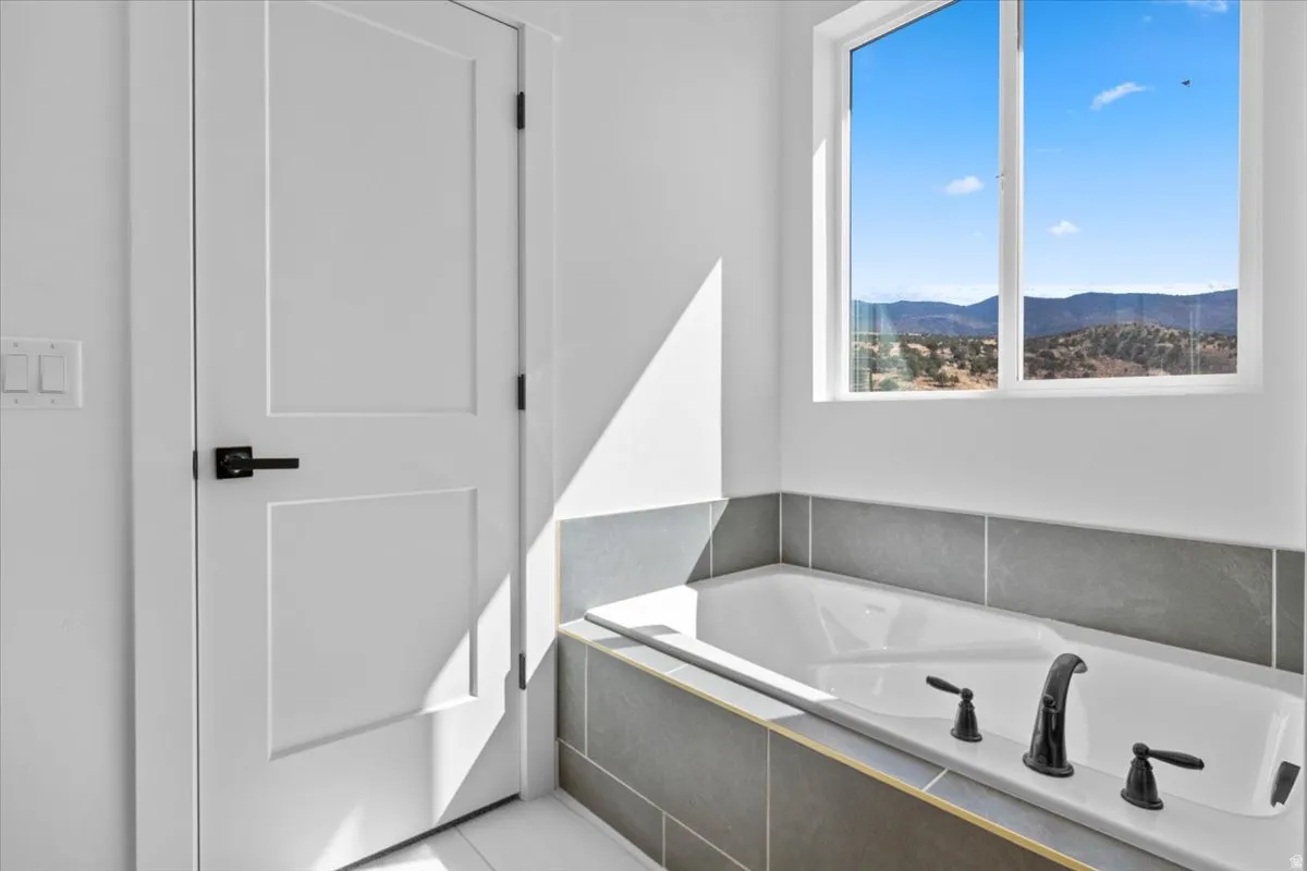 Integrated soaking tub with gray tile surround, matte black fixtures, and a large window