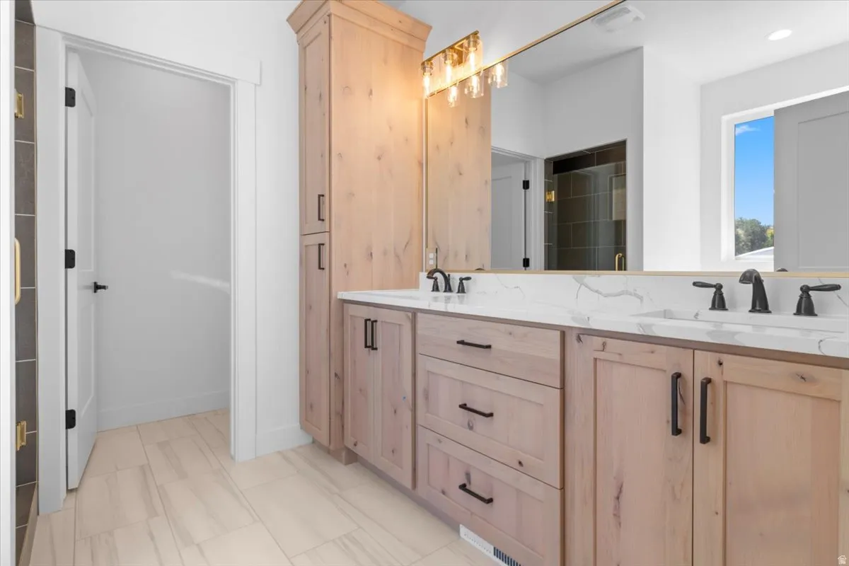Dual vanity with light wood-finish cabinetry, quartz countertops, and matte black fixtures