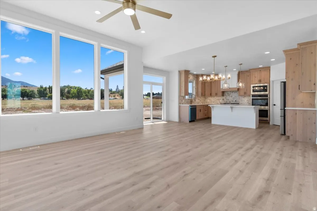 Open-concept living area featuring light wood-finish flooring, a contemporary ceiling fan, and large windows