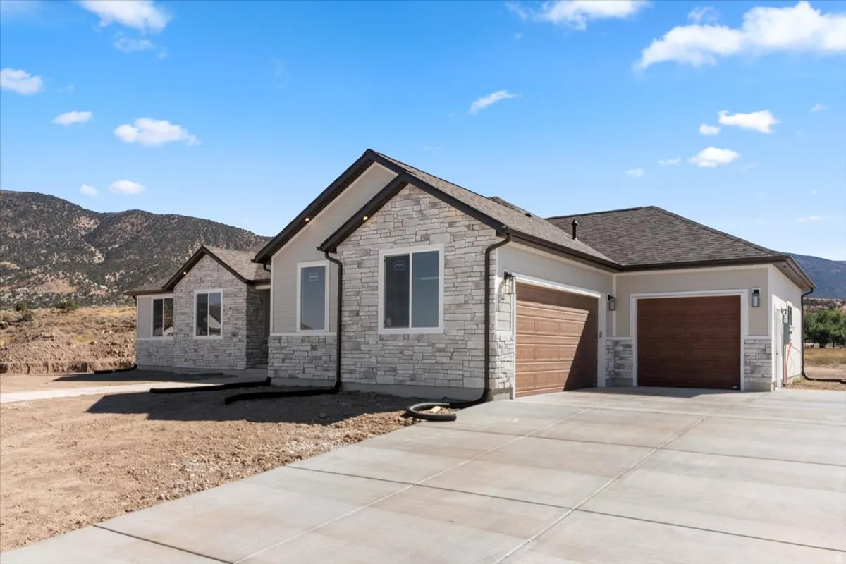 Stucco and stone exterior with a concrete driveway and attached garages featuring wood-finish doors