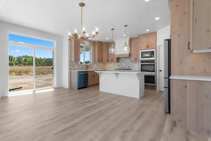 Expansive wood-finish flooring, sliding glass doors, contemporary chandelier, kitchen island with seating, and stainless steel appliances
