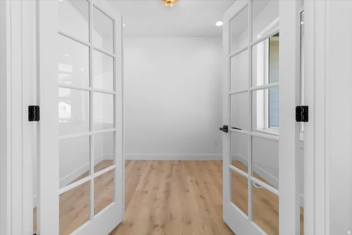 French doors with matte black hardware, wood-finish flooring, and a window for natural light