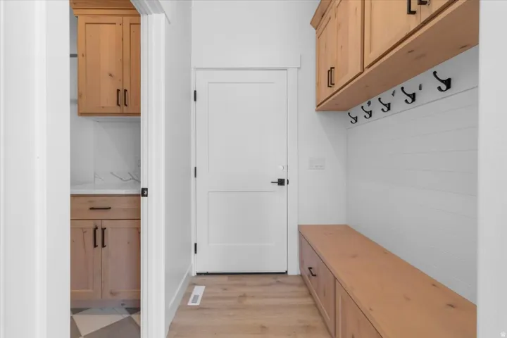 Hardwood flooring, built-in wooden bench with storage, wooden upper cabinetry, white shiplap wall paneling, and black wall hooks