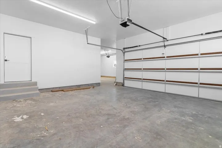 Concrete flooring, bright white walls, overhead lighting, garage door opener system, interior access door