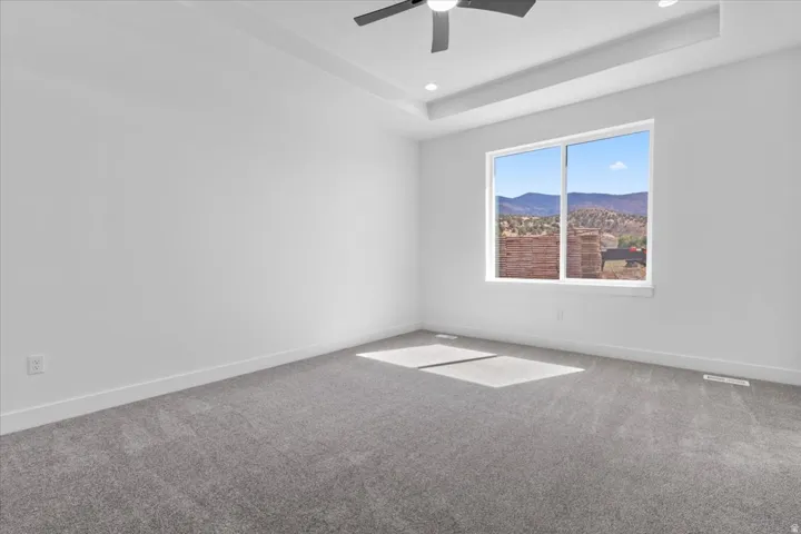 Bright interior with grey carpet flooring, a large window showcasing a mountain landscape, and a contemporary ceiling fan