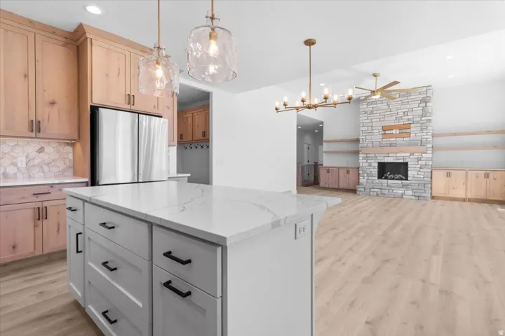 Kitchen island with a light-toned countertop, wood-finish flooring, and a stone-clad fireplace