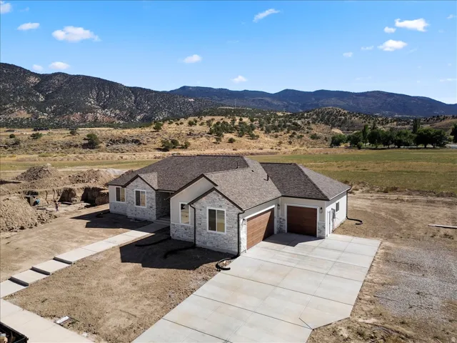 Stone and stucco exterior with a dark-tone shingle roof, wood-finish garage doors, concrete driveway, and mountain backdrop