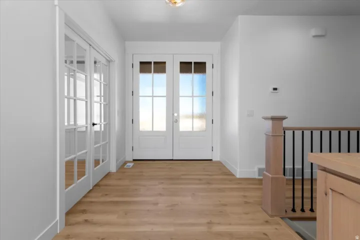 Wood-finish flooring throughout, white framed French doors with divided lites, white framed entry doors with frosted glass, light wood newel post and railings, and black metal balusters