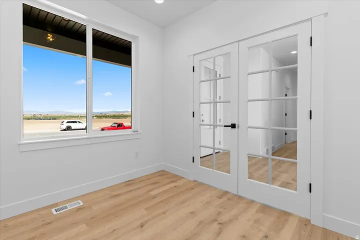 French doors with glass panels, light wood-finish flooring, white walls, recessed lighting, and a large window