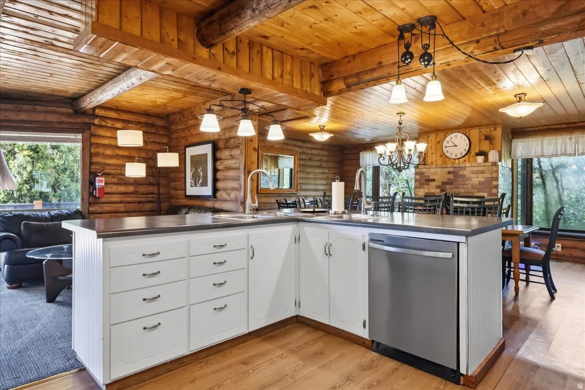 Extensive wood paneling throughout, wood-finish flooring, white cabinetry, stainless steel dishwasher, and a built-in kitchen island with a sink