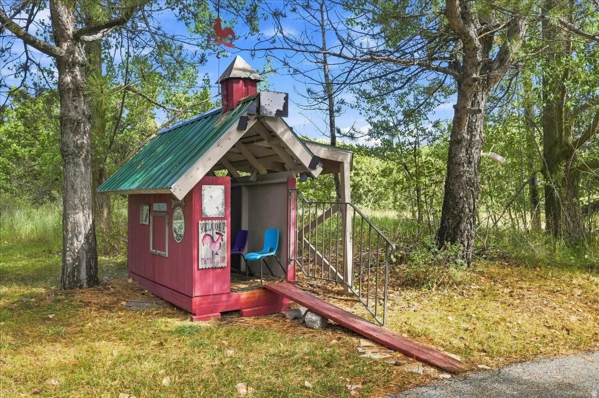 Red playhouse structure featuring a green metal roof, a covered porch, and a small cupola