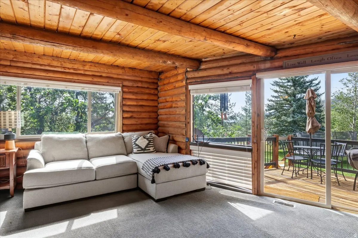 Wood-paneled ceiling with exposed beams, log wall construction, large window with natural light, glass sliding door, and outdoor wooden deck