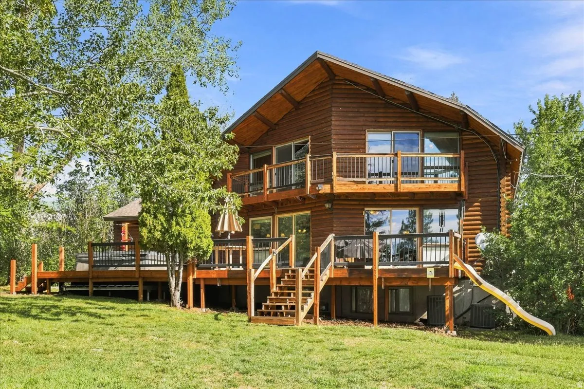 Multi-level wood-sided residence with multiple outdoor decks, a ground-level patio, and a sloped grass lawn