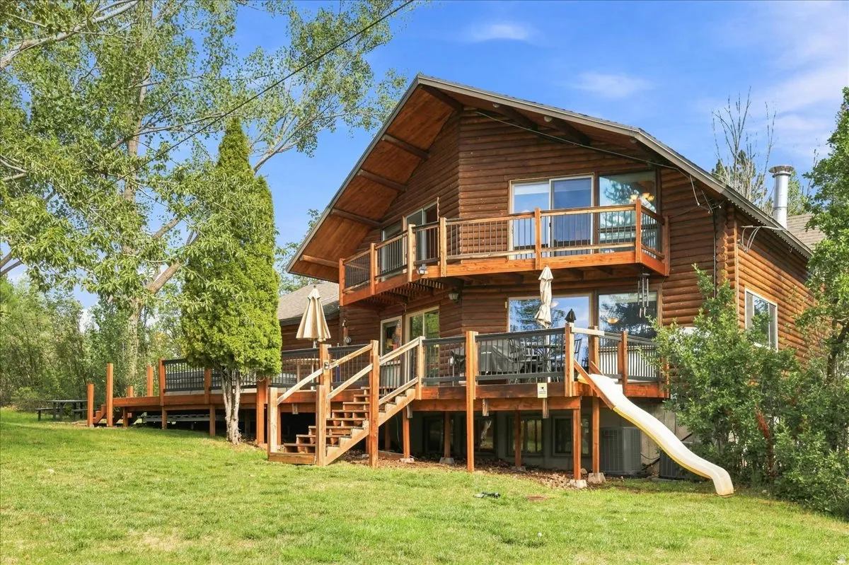 Log cabin exterior with multiple wooden decks, a second-story balcony, and a manicured lawn