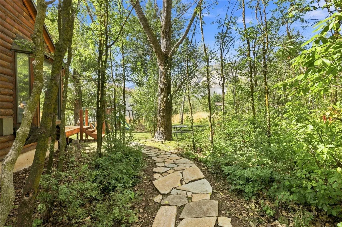 Log cabin exterior, stone pathway, mature trees, wood deck, natural landscaping