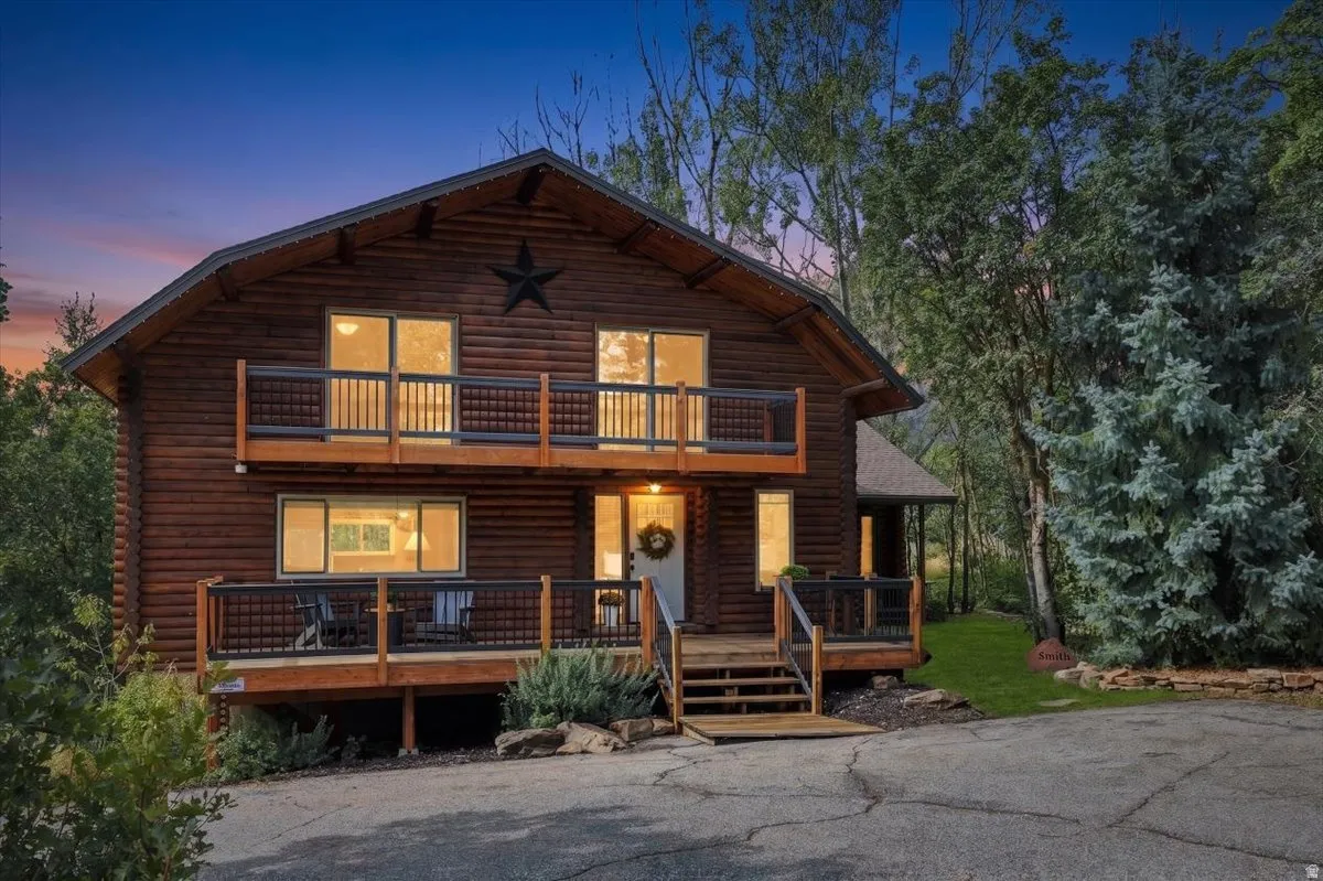 Log cabin exterior with an A-frame roofline, featuring two levels of balconies with dark railings, multiple windows, and a prominent front entry with wooden steps
