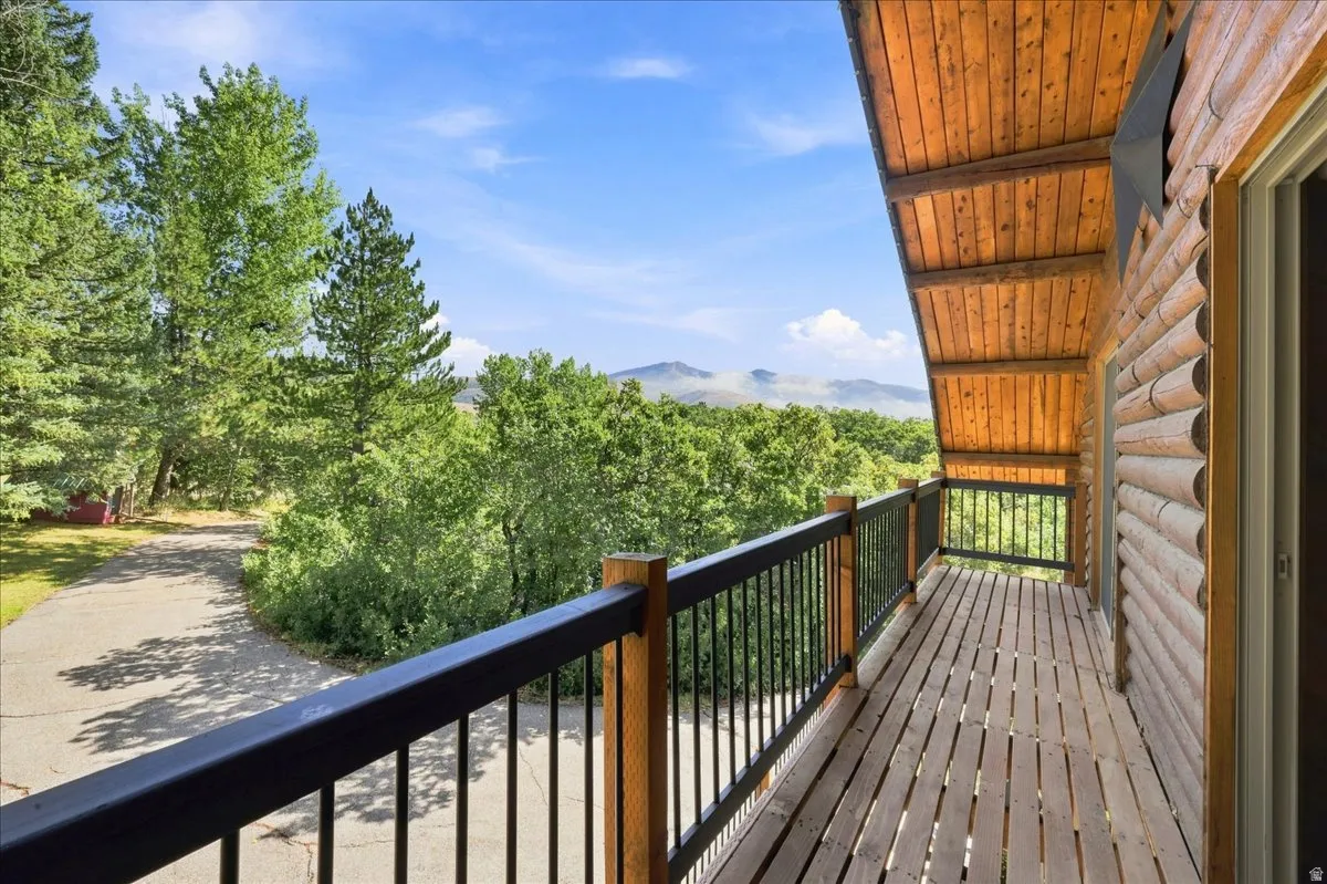 Expansive wood deck with black metal railings, log-style exterior, exposed wood ceiling, and surrounding mature trees