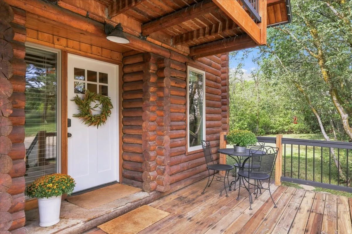 Log-style exterior featuring a front porch with wood plank flooring, white entry door with glass panels, and a metal railing