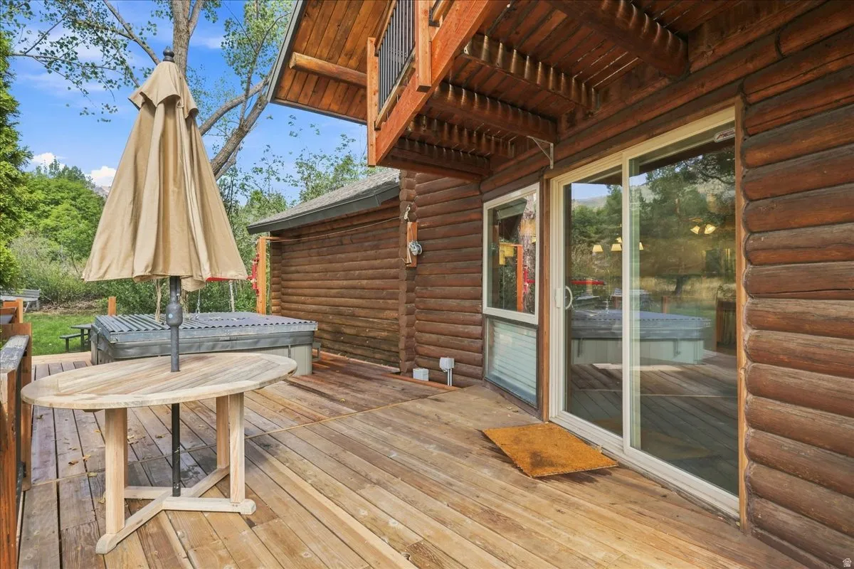 Expansive wood deck with a built-in hot tub, log siding exterior, and sliding glass door access