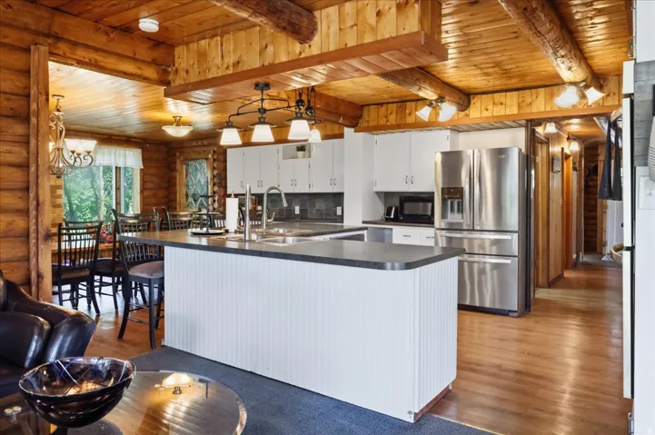 Kitchen featuring an island with a sink, white cabinetry, stainless steel appliances, and wood-finish flooring