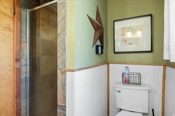 Glass-enclosed shower with tiled surround, white toilet, and wainscoting with wood trim