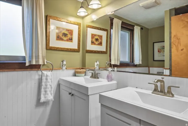 Dual vanity with integrated sinks, brushed nickel fixtures, white cabinetry, and beadboard wainscoting