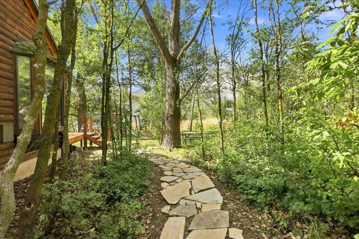 Log cabin exterior, stone pathway, mature trees, wood deck, natural landscaping