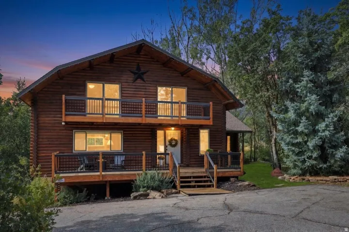 Log cabin exterior with an A-frame roofline, featuring two levels of balconies with dark railings, multiple windows, and a prominent front entry with wooden steps