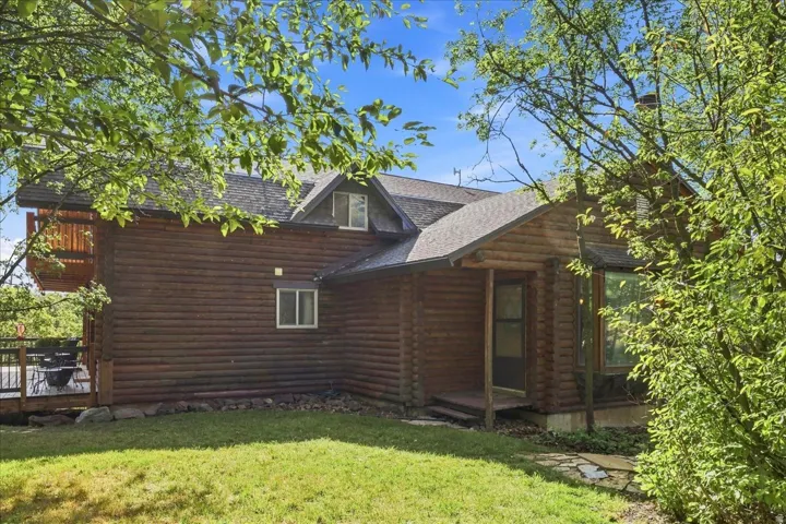 Log cabin exterior with an asphalt shingle roof, dormer window, and a wood-planked deck