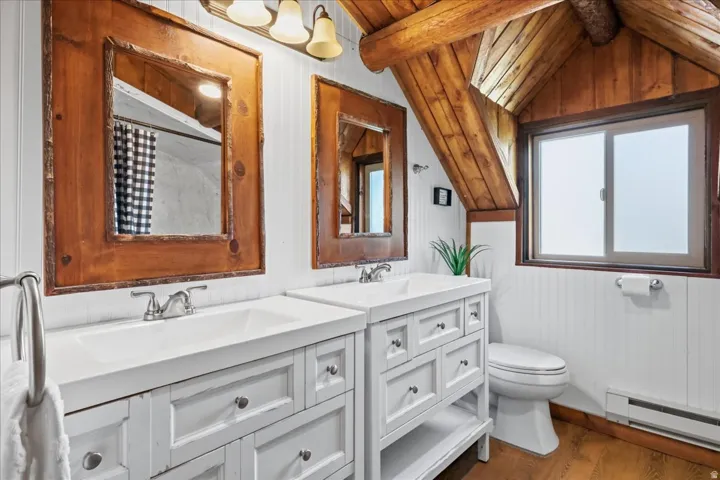 Dual white vanities with integrated sinks, wood-framed mirrors, wood-paneled ceiling, white vertical paneling, and wood-finish flooring