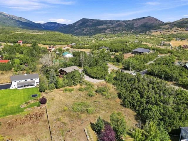 Expansive lot with mountain backdrop, surrounded by lush greenery and scattered residential properties
