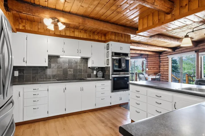 Wood-finish flooring, white cabinetry, dark tiled backsplash, stainless steel double wall ovens, and wood-paneled ceilings