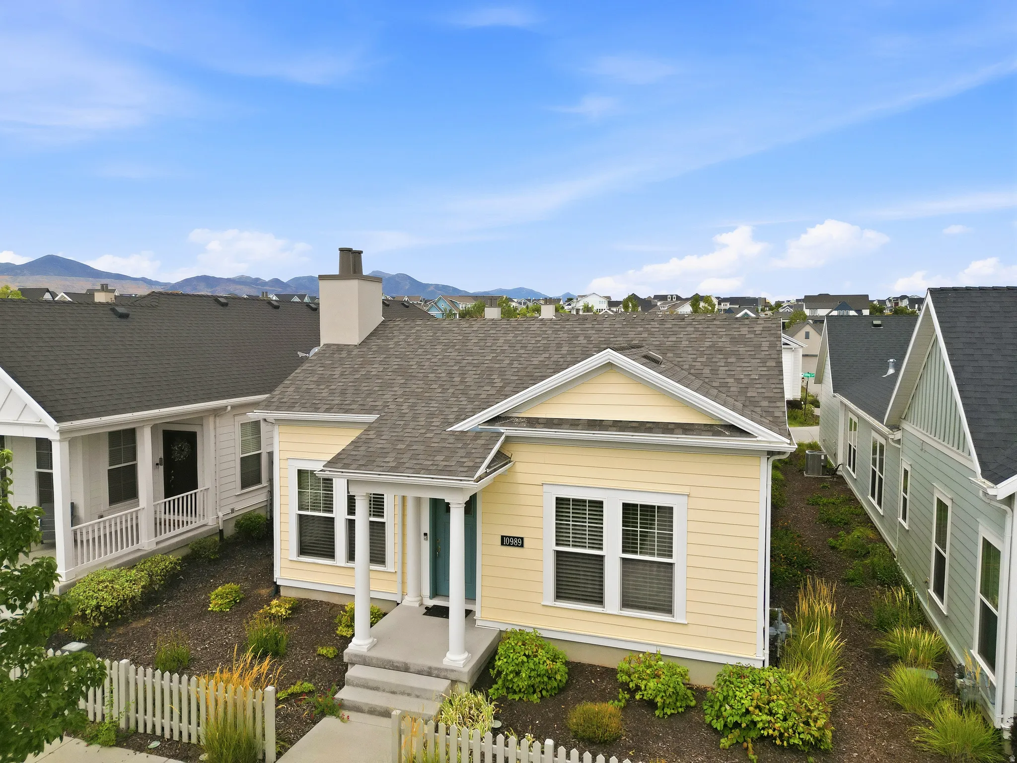 Yellow exterior siding, covered entryway, white picket fence, chimney structure, and dark shingle roof