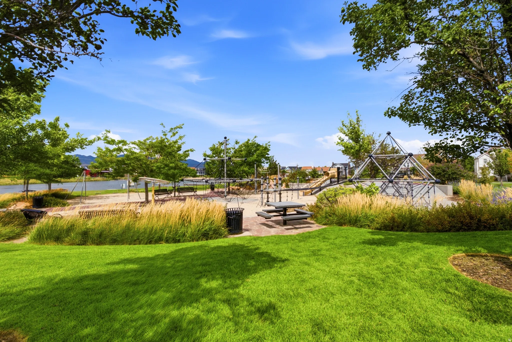 Expansive park space featuring a manicured lawn, playground structures, a picnic area with a built-in table, and mature landscaping