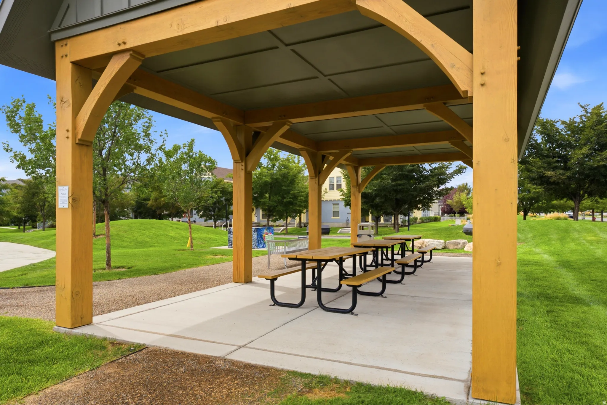 Expansive outdoor pavilion with exposed timber framing and concrete flooring, surrounded by lush green landscaping