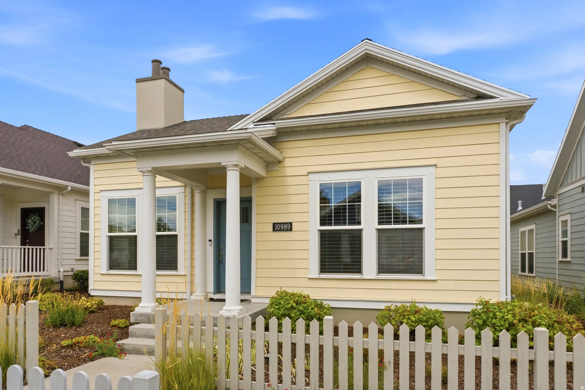 Yellow horizontal siding exterior with a covered entry, white picket fence, and a chimney feature