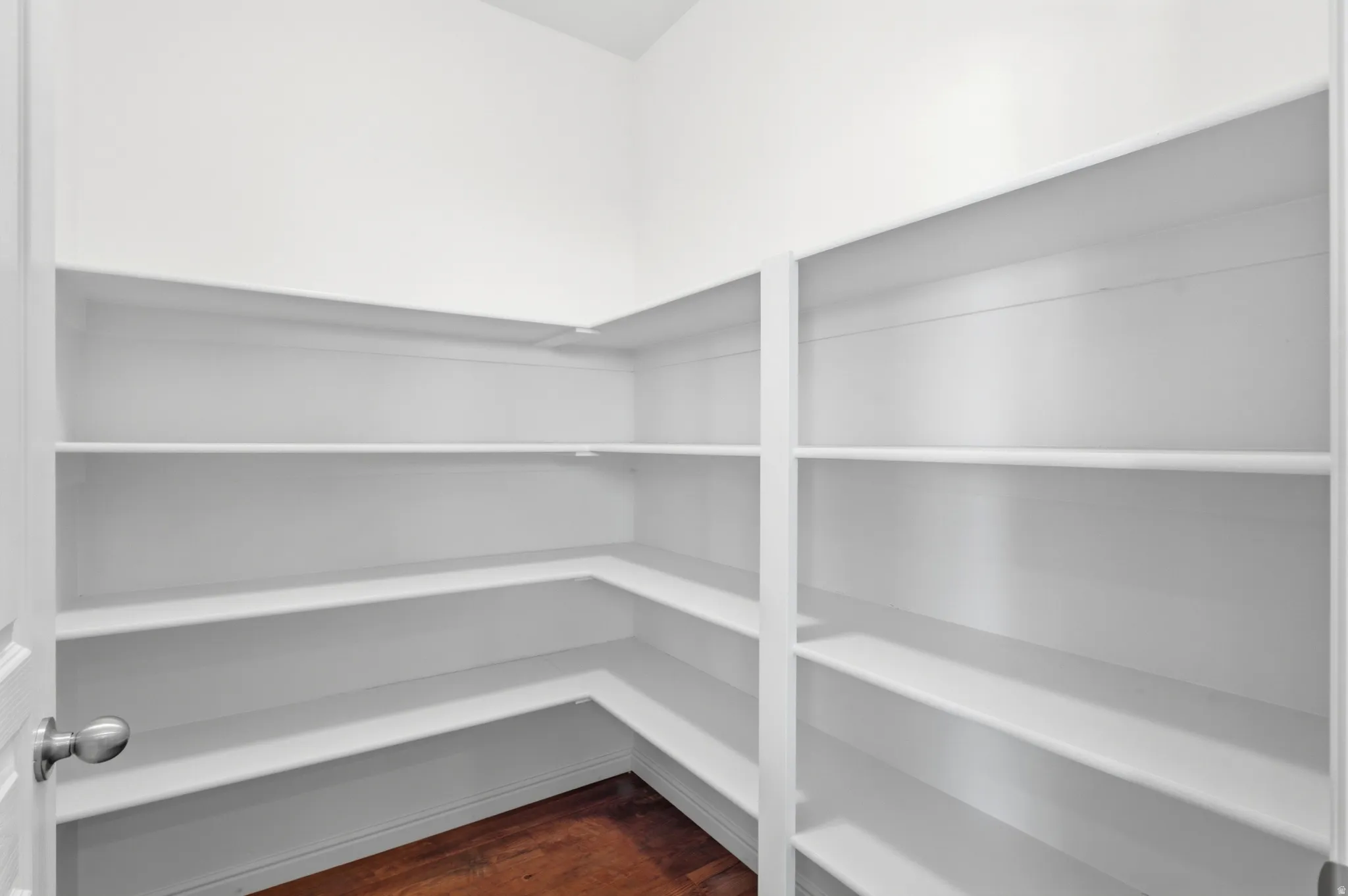Walk-in pantry featuring white built-in shelving, white walls, and wood-finish flooring