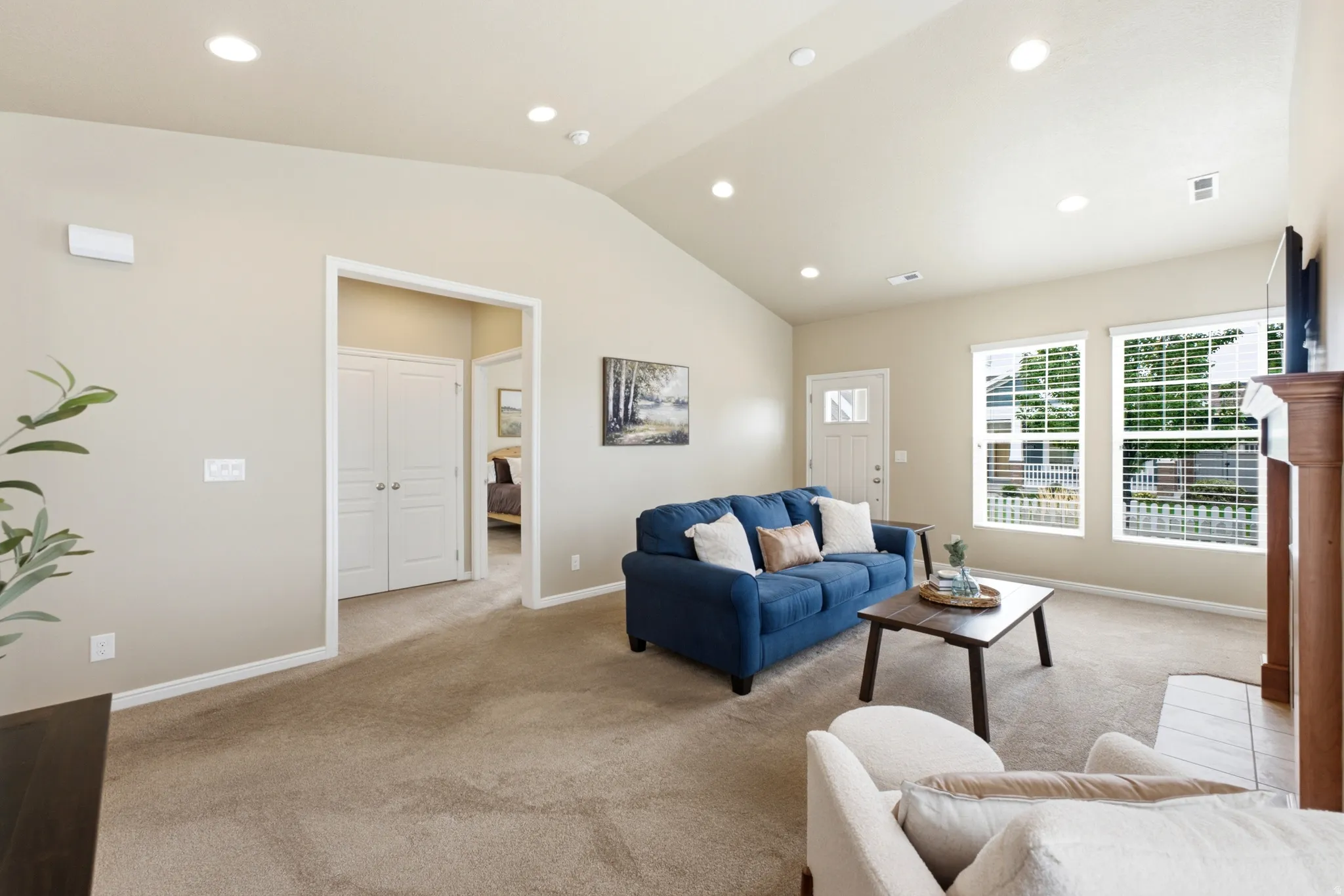 Vaulted ceiling with recessed lighting, carpeted flooring, multiple windows, and a wood-finish mantel