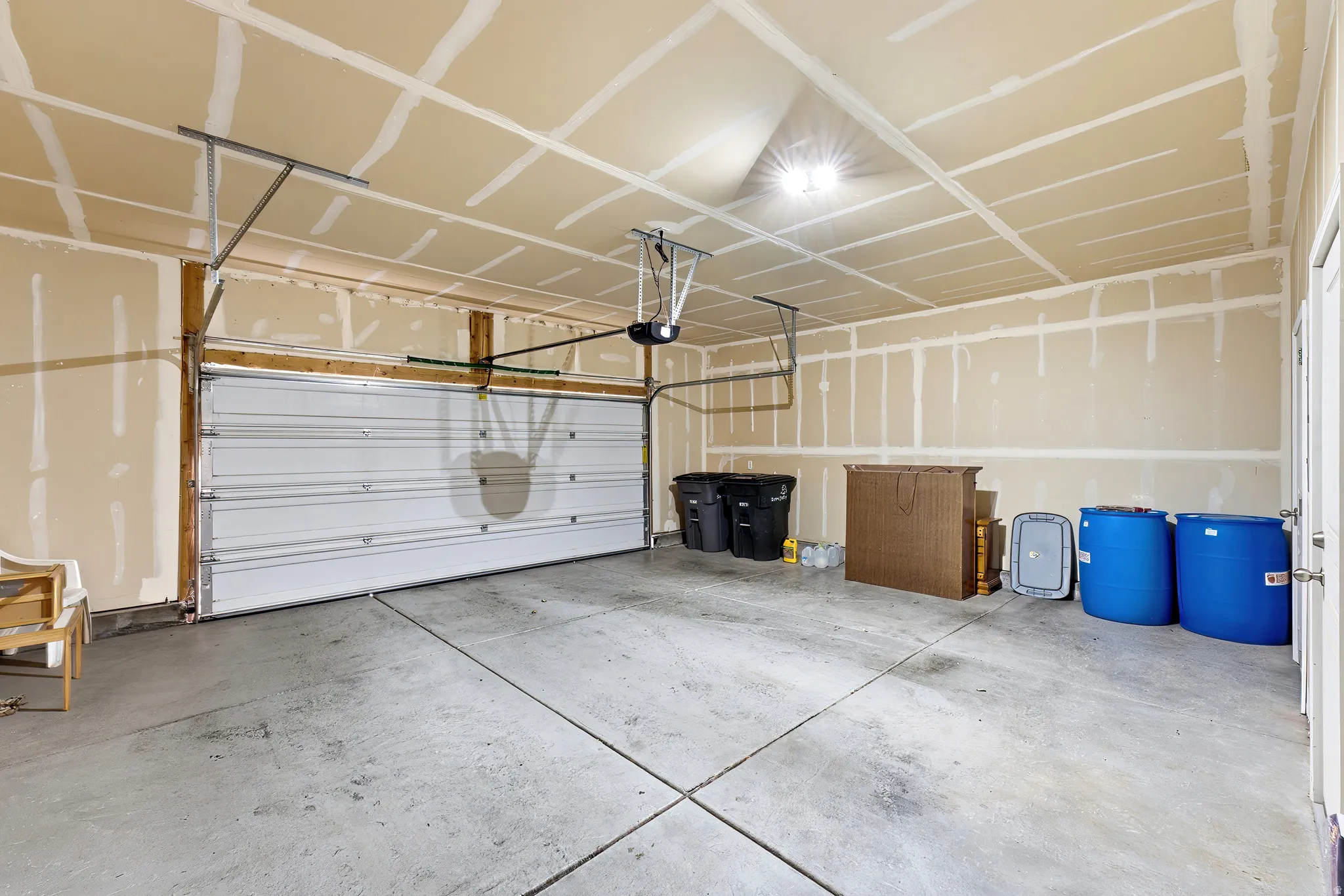Concrete flooring, exposed stud walls, overhead lighting, garage door, and entry door