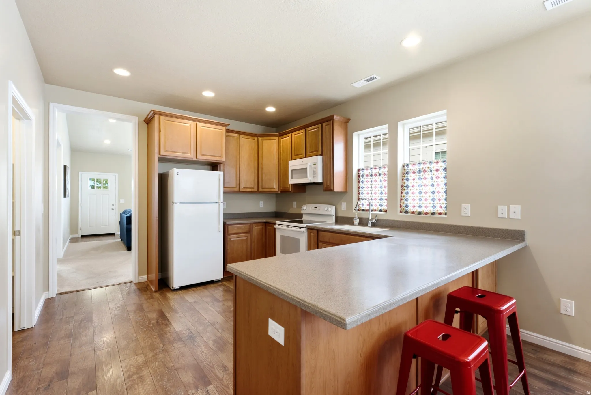 Kitchen featuring wood-finish flooring, recessed lighting, wood cabinetry, built-in appliances, and a peninsula with a light-toned countertop