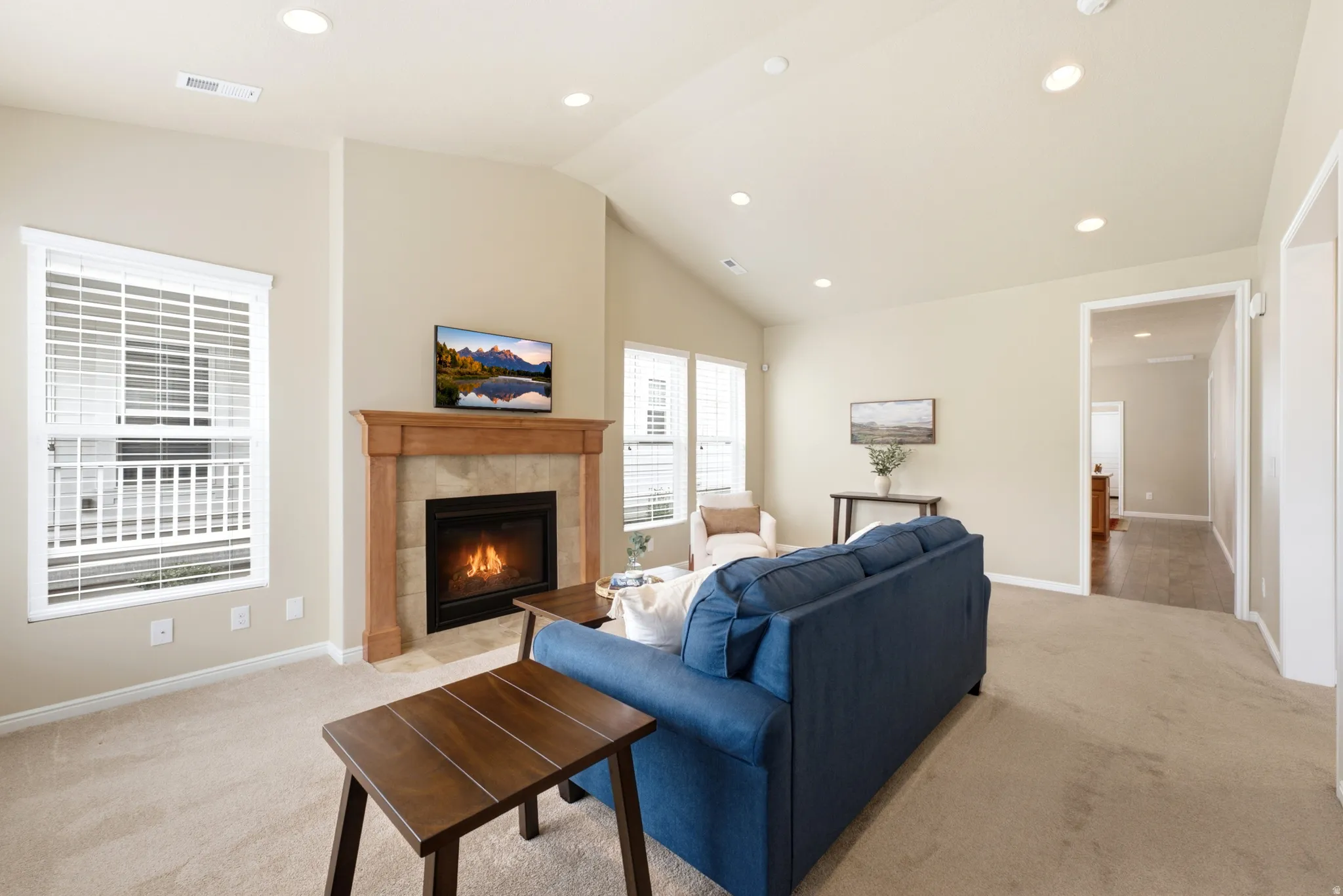 Recessed lighting, vaulted ceiling, wood-surround fireplace with tile accents, carpeted flooring, and a window with blinds