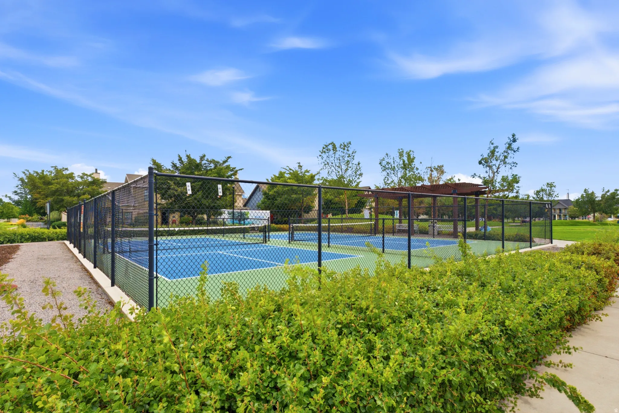 Fenced recreational courts with a blue and green surface, bordered by landscaping and a gravel path