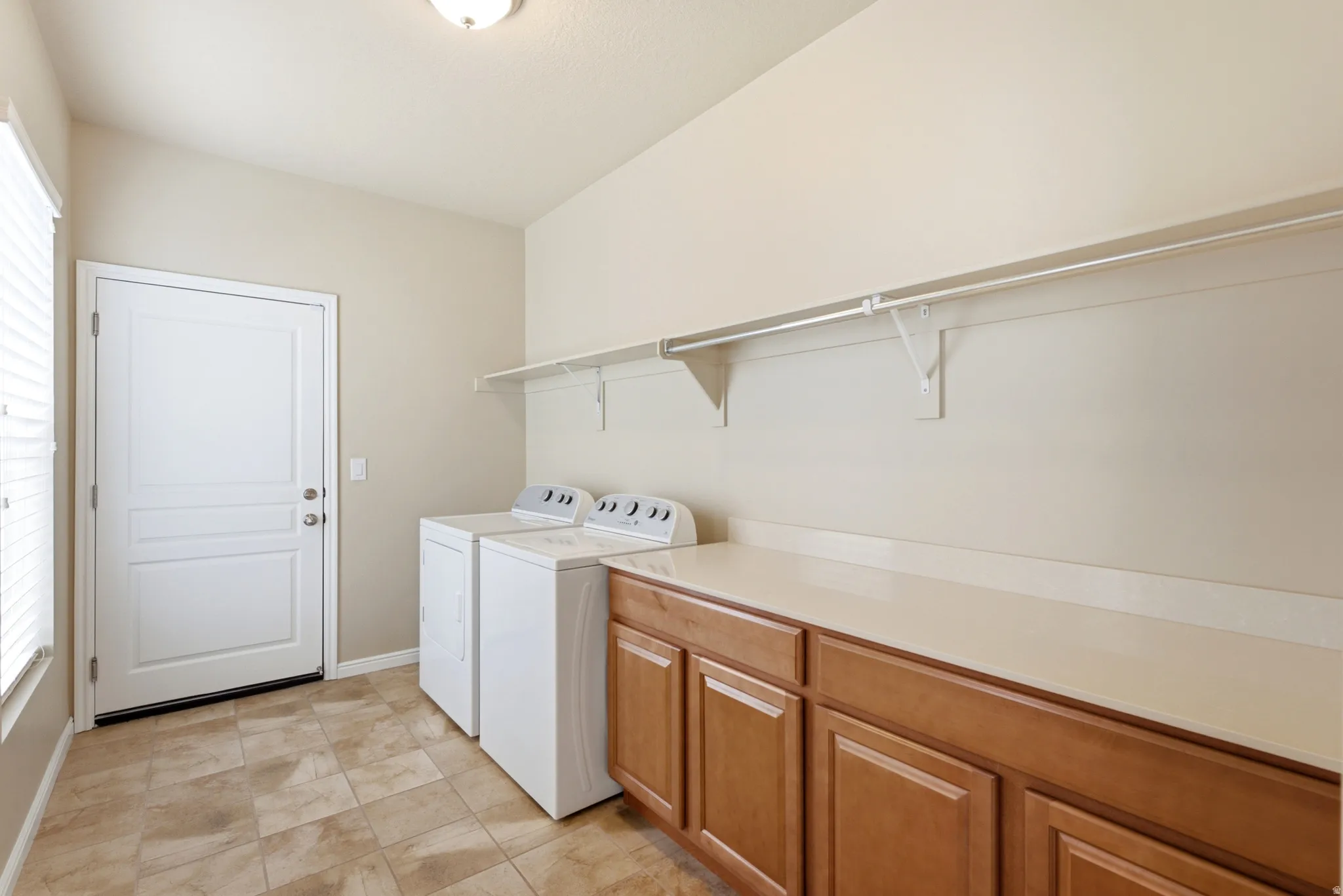 Tile flooring, wood-finish cabinetry, solid surface countertop, white shelving, and a prominent window with blinds