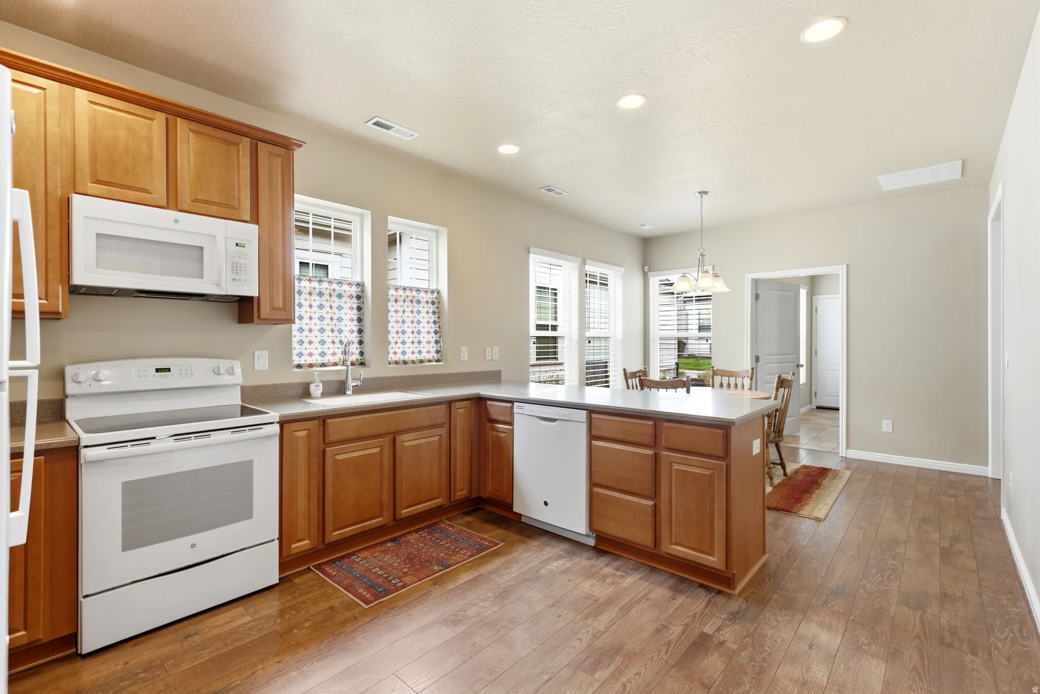 Kitchen featuring wood-finish flooring, recessed lighting, white appliances, and warm wood cabinetry