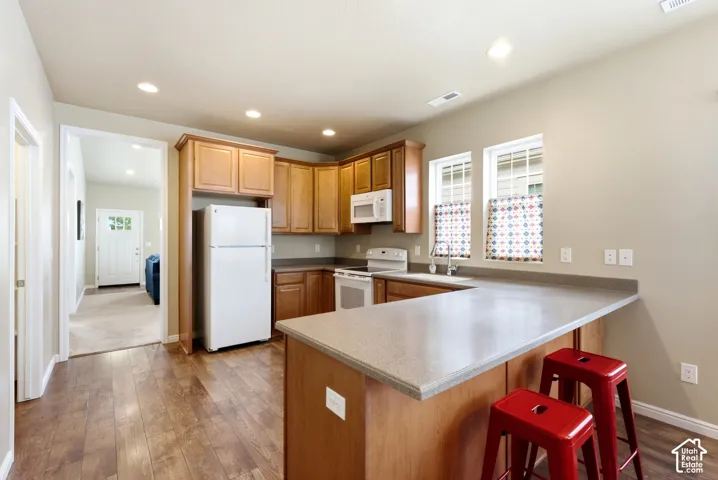 Kitchen featuring wood-finish flooring, recessed lighting, wood cabinetry, built-in appliances, and a peninsula with a light-toned countertop