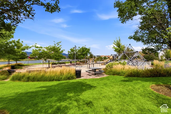 Expansive park space featuring a manicured lawn, playground structures, a picnic area with a built-in table, and mature landscaping