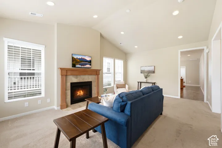 Recessed lighting, vaulted ceiling, wood-surround fireplace with tile accents, carpeted flooring, and a window with blinds