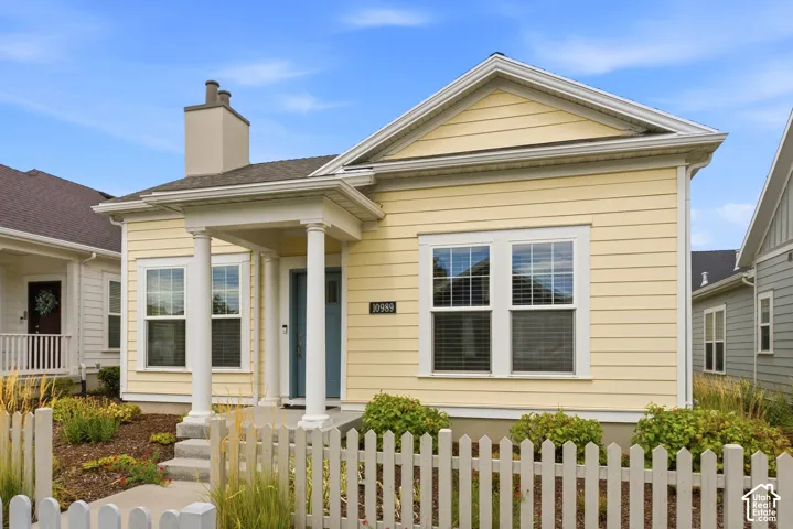 Yellow horizontal siding exterior with a covered entry, white picket fence, and a chimney feature
